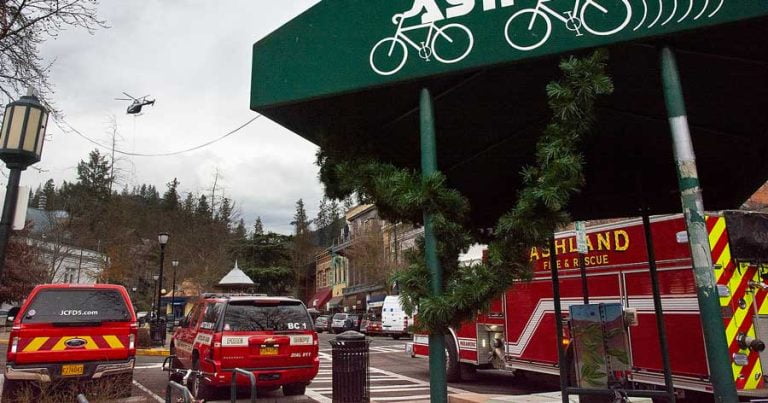 Ashland Fire & Rescue vehicles, at center and right, along with a Jackson County Fire District No. 5 vehicle, at left, stand by at Ashland Plaza on Tuesday, Jan. 11, while a helicopter carries a ventilation unit to the top of an Oregon Shakespeare Festival theater. Drew Fleming photo