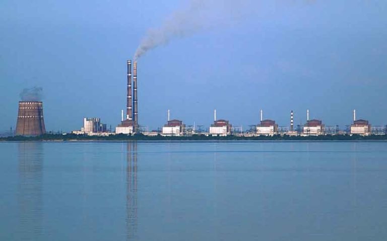 Two power stations at Enerhodar, about 50 km from Zaporozhye in Ukraine, viewed from across the Kakhovka Reservoir on the river Dnieper. Photo taken from the “Nikopol” shore. The nearer power station is Zaporizhzhia Nuclear Power Plant, the biggest nuclear power station in Europe, consisting of two cooling towers (one largely obscured by the other) at the left and six VVER reactor buildings. Image via Wikimedia by Ralf1969 used under terms of the GNU Free Documentation License