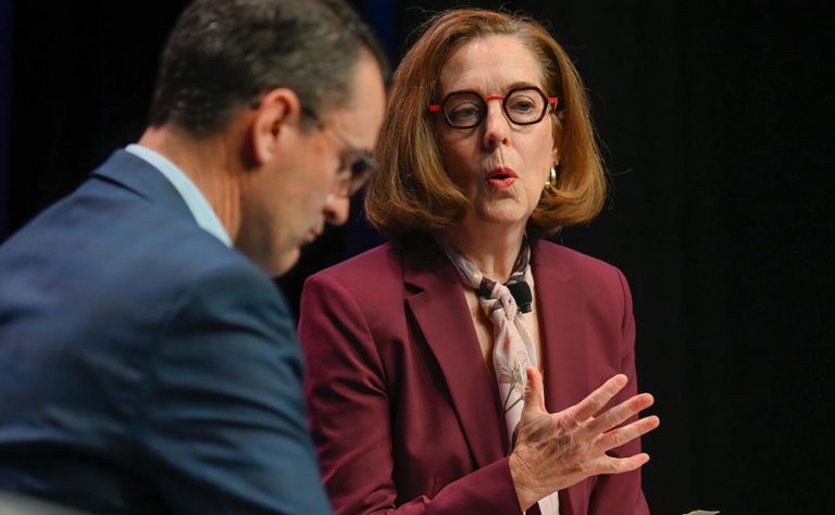 Gov. Kate Brown speaks with Dutch Bros CEO Joth Ricci at the Oregon Business Plan summit in Portland in December 2021. Oregon Capital Chronicle photo by Ron Cooper