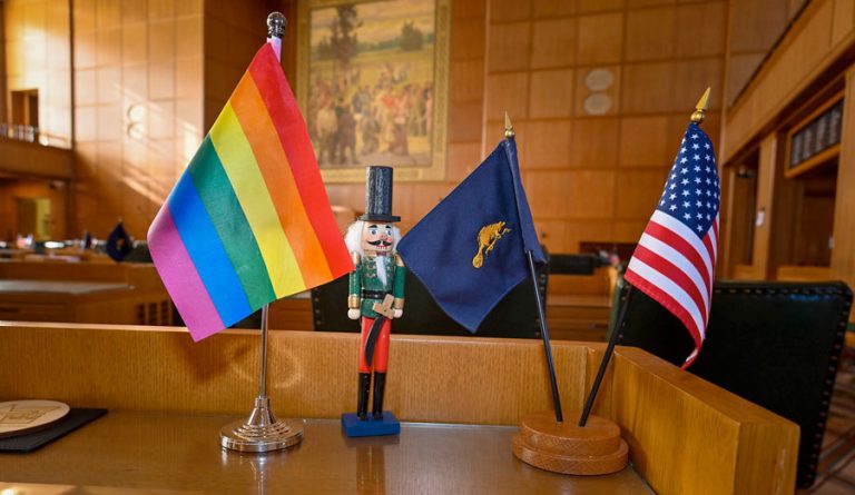 A Pride flag, Oregon flag and U.S. flag rest on a desk in the Oregon Capitol. Oregon Capital Chronicle photo by Ron Cooper