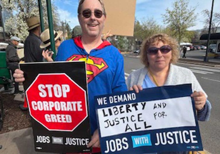 Demonstrators Jason and Vanessa Houk hold up signs during the "Hands Off" rally on Ashland Plaza on Saturday morning. Debora Gordon photo for Ashland.news