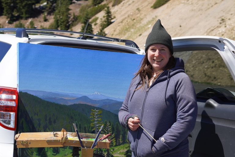 Sarah F. Burns, the Siskiyou Crest Coalition’s first Acorn Woman Lookout Artist in Residence, poses with a picture of Mt. Shasta. Photo courtesy of Sarah F. Burns.