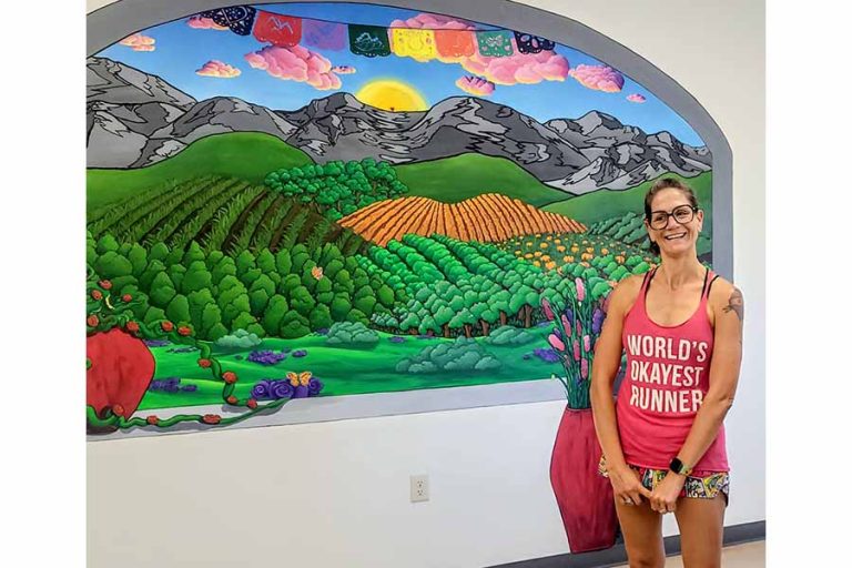 Artist Sarah Bernard stands beside the mural she created for OHRA's cafe that serves the homeless and hungry. Art Van Kraft photo